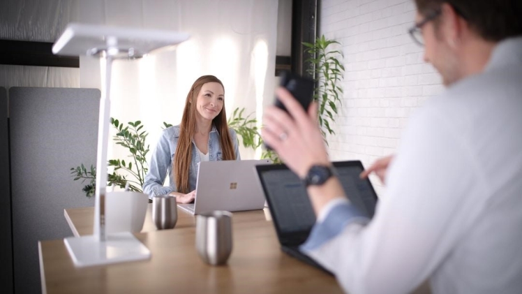 Two employees sitting at their desks discussing how to make an area chart on their laptops
