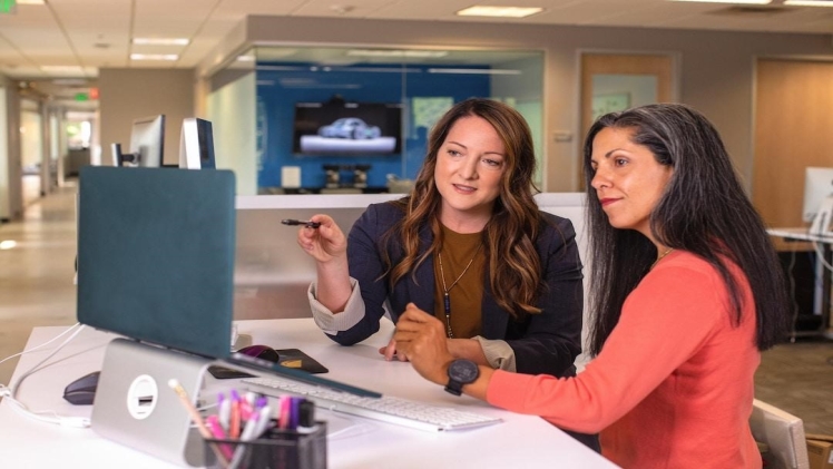 Businesswoman teaching her coworker how to make an area chart while they both sit at a desk